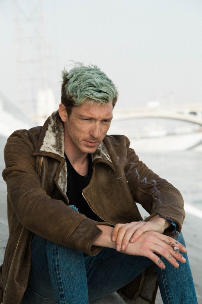 Au bout de combien de temps un homme regrette d’avoir rompu ? man with green hair in black shirt and brown coat sits on brown sand near white suspension bridge