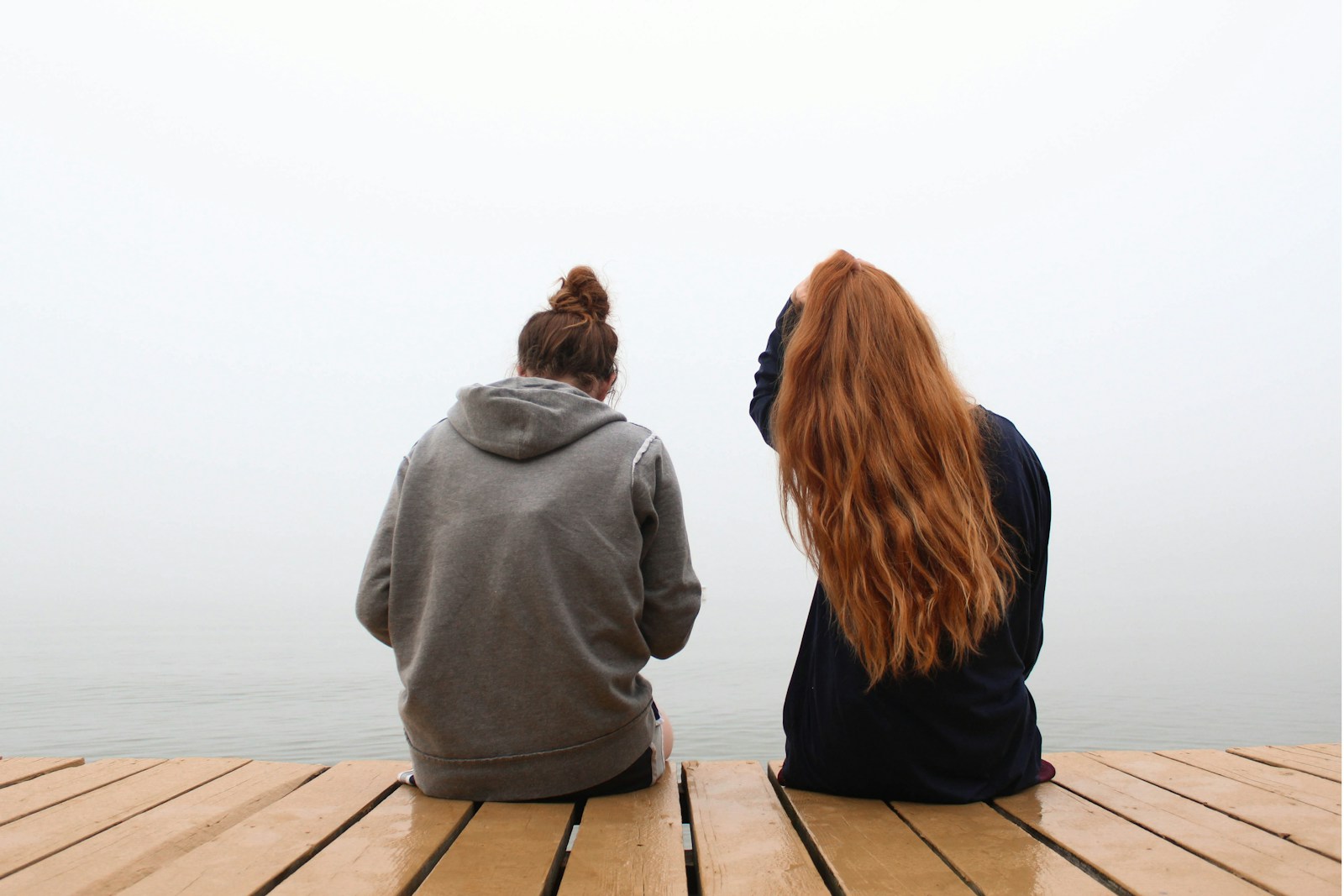 two women sitting on wooden dock over body of water