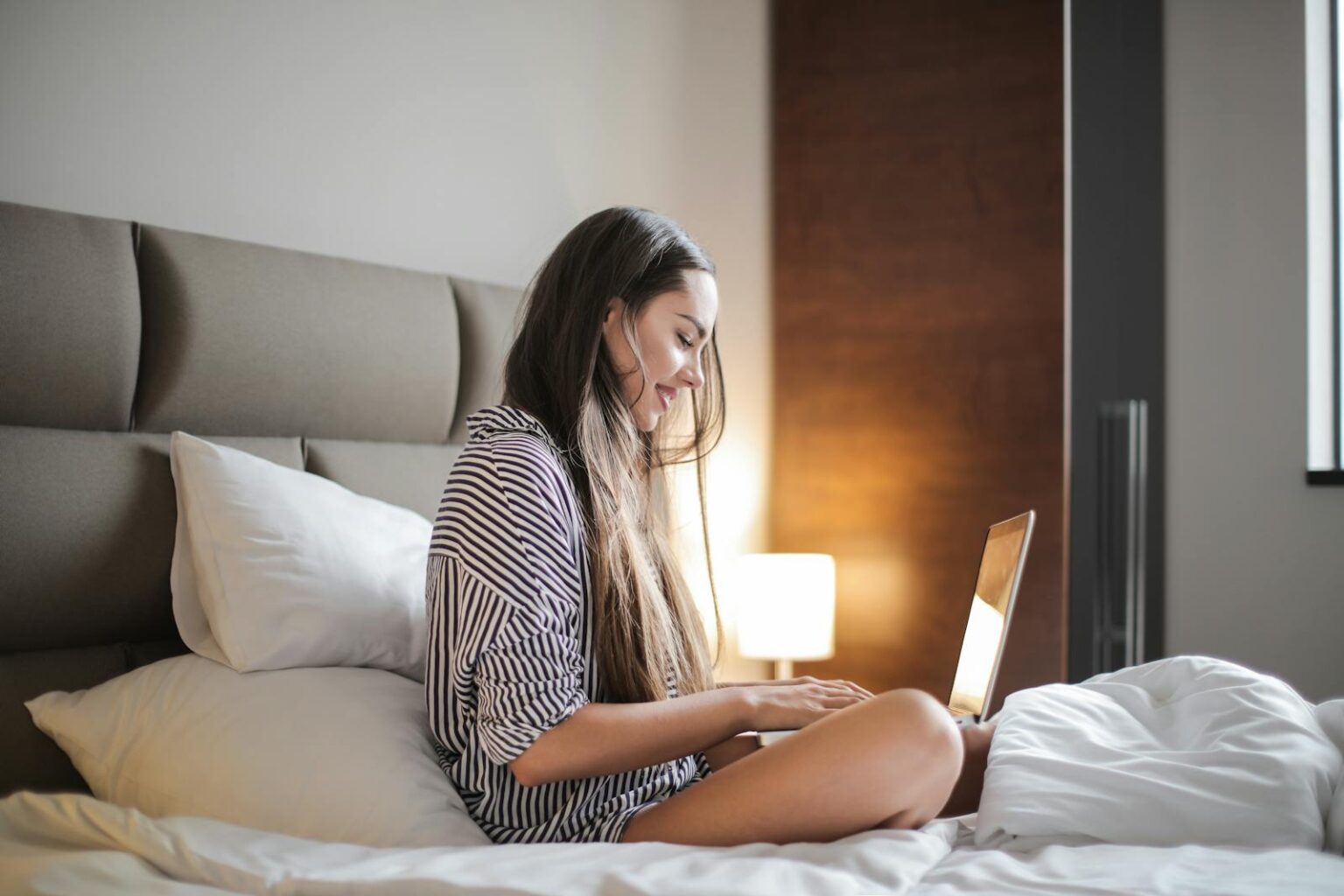 Les meilleurs sites de rencontre sérieux pour trouver l’amour Side View Photo of Smiling Woman in a Black and White Striped Top Sitting on a Bed While Using a Laptop