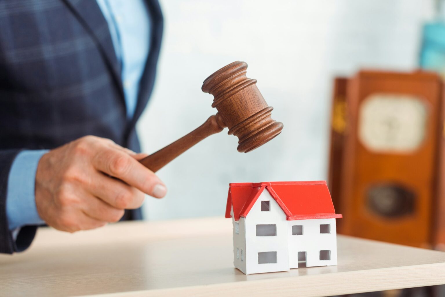 Comment acheter un bien immobilier aux enchères ? cropped view of auctioneer hitting model of house with gavel during auction