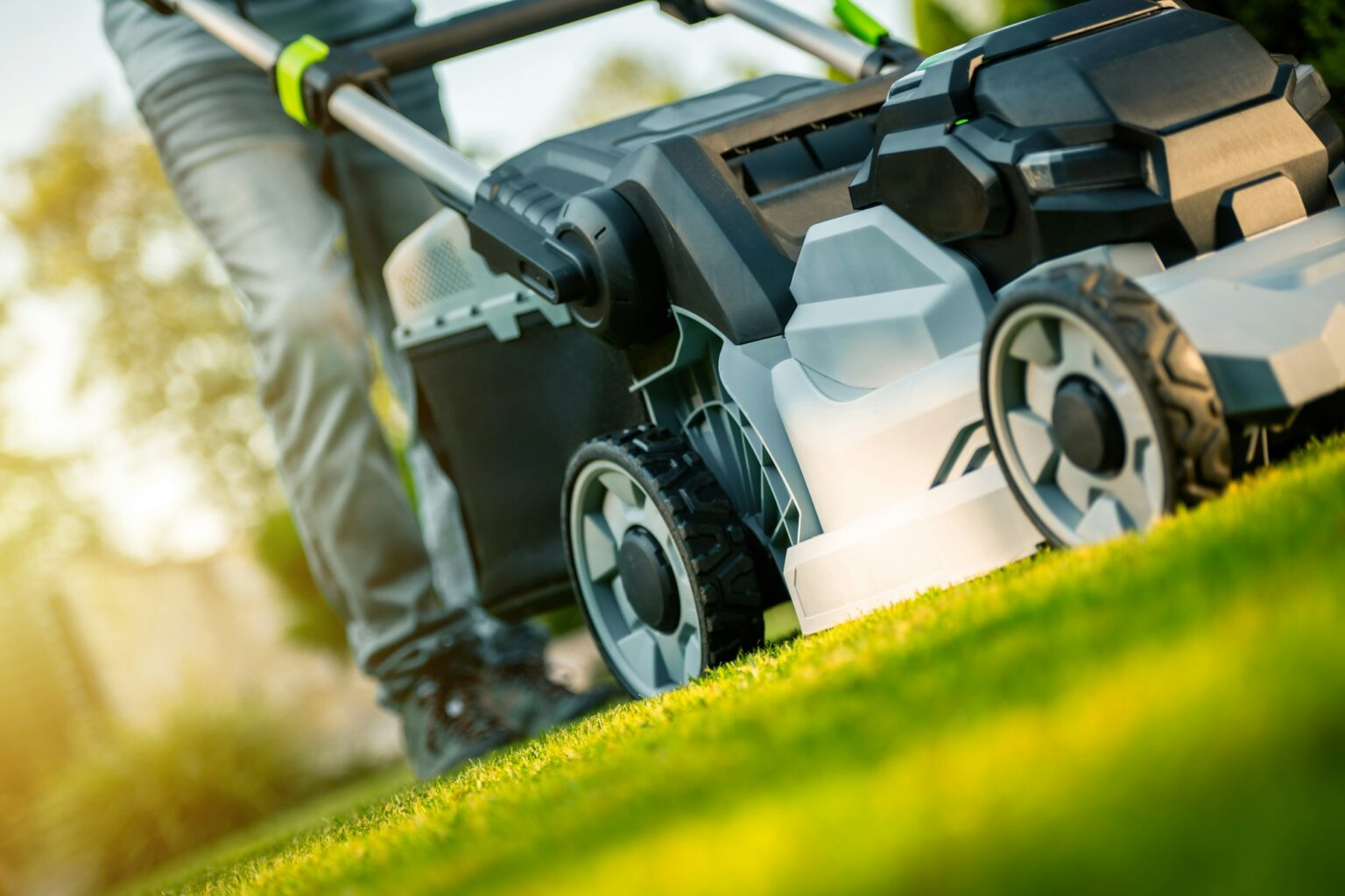 Man Mowing a Lush Green Lawn in the Afternoon Sunlight Using a Modern Lawnmower