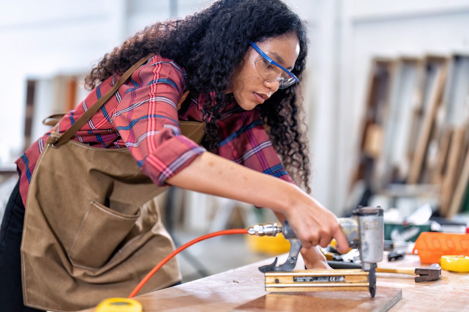In work place carpenter girl concentrate working using pneumatic nail gun drive nail to the wood